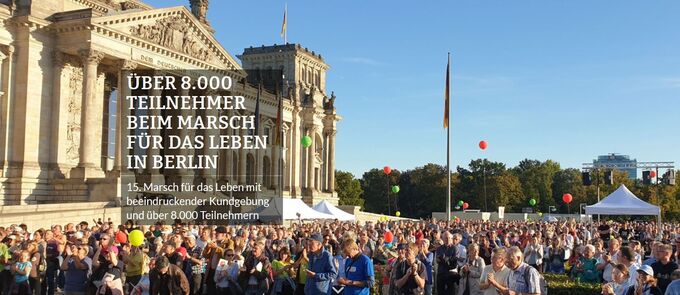 Eine große Menschenmenge versammelt sich vor einem historischen Gebäude in Berlin. Viele Teilnehmer halten bunte Luftballons und applaudieren. Im Hintergrund sind Zelte und Fahnen zu sehen. Ein Banner informiert über den Marsch für das Leben mit über 8.000 Teilnehmern.