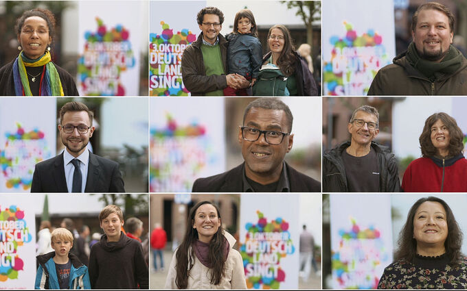 Eine Collage von neun Porträts verschiedener Personen, die lächeln und vor einem bunten Hintergrund mit dem Text "Oktober Deutschland singt" stehen. Die Personen sind unterschiedlich alt und ethnisch, und sie strahlen Freude und Gemeinschaft aus.