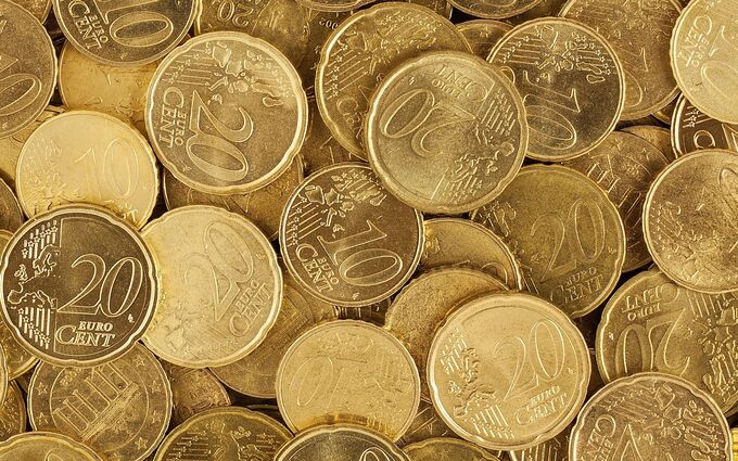 Eine Ansammlung von Euro-Münzen, hauptsächlich 20-Cent-Münzen, die dicht nebeneinander liegen. Einige 10-Cent-Münzen sind ebenfalls sichtbar. Die Münzen sind in verschiedenen Winkeln angeordnet und reflektieren das Licht.